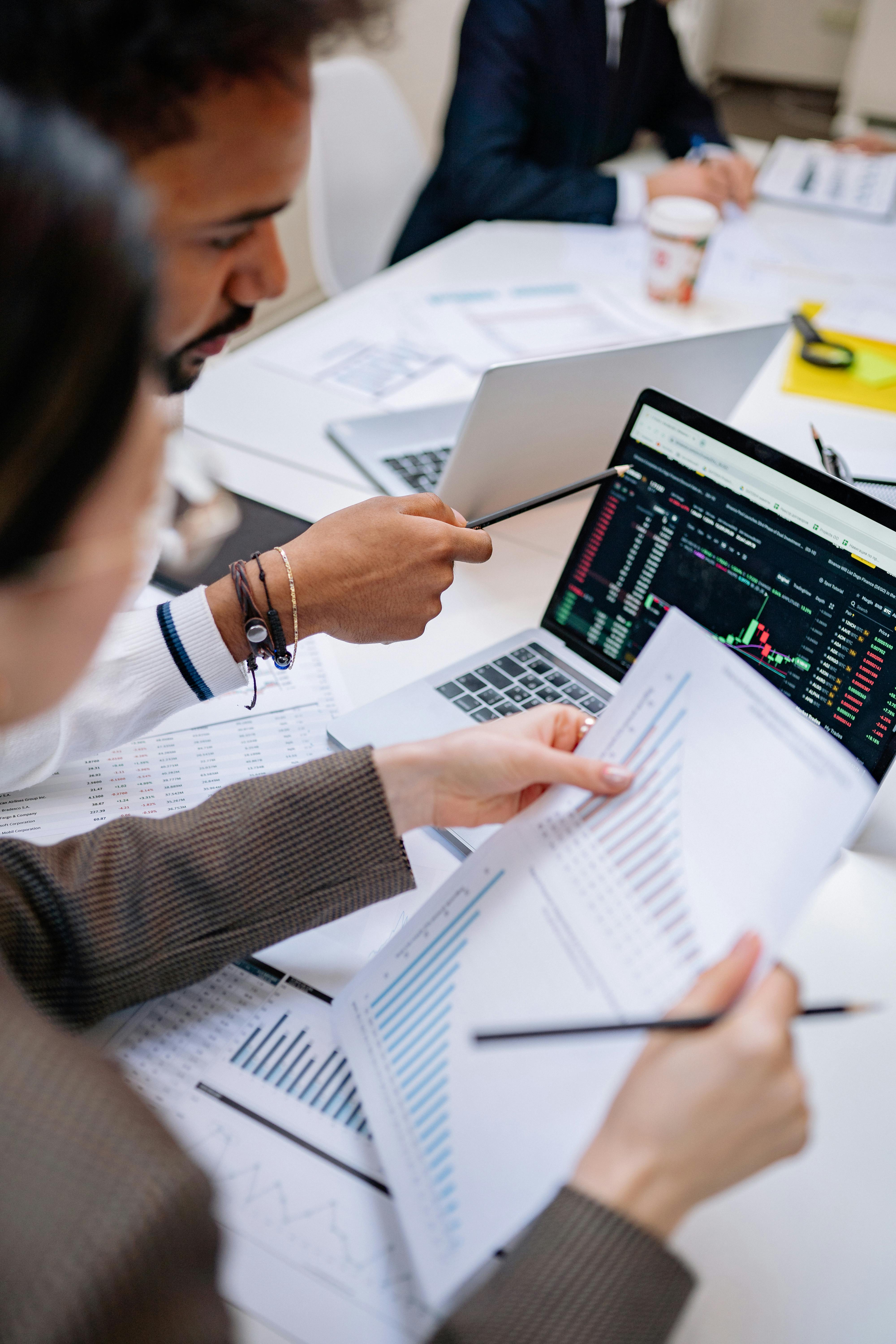 People reviewing financial sheets and charts with laptops in an office setting
