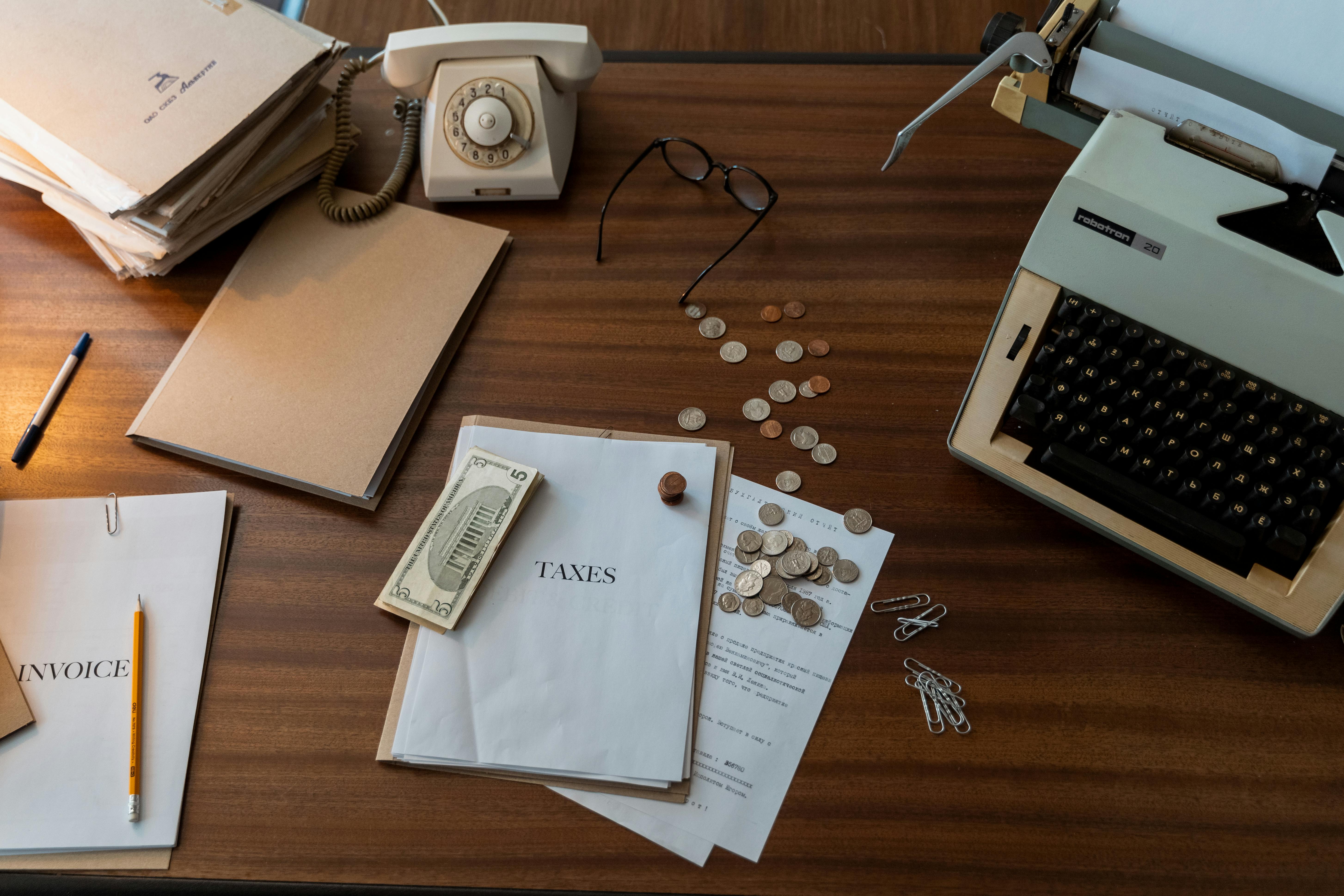 Top view workspace with invoice papers, coins, and typewriter on a wooden table